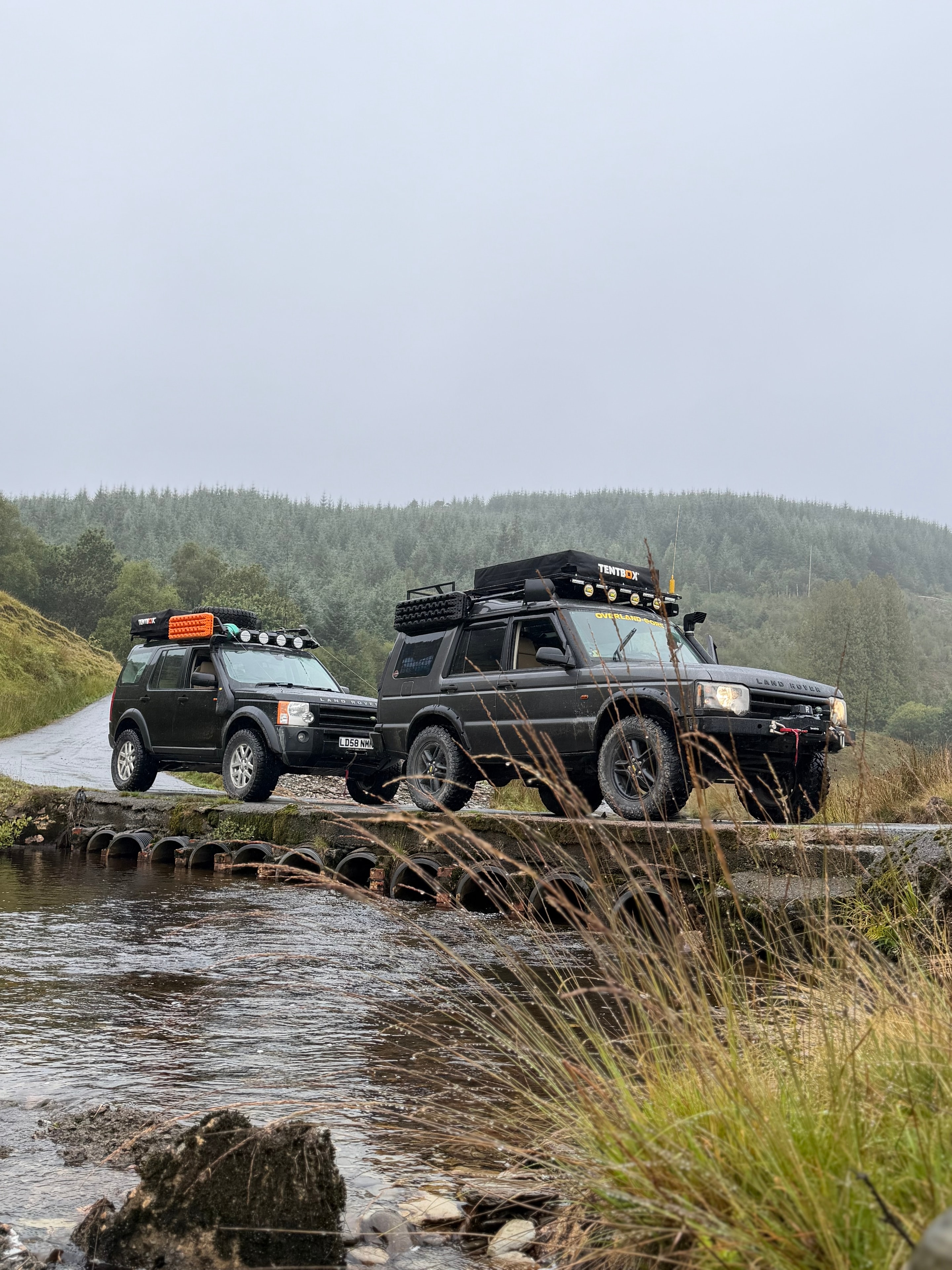 Two Land Rovers crossing a river ford in Wales